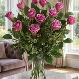 Pink roses arranged in a clear glass vase with mixed greenery