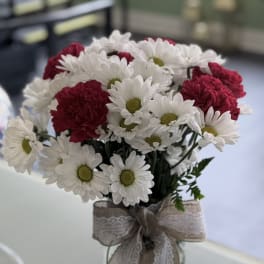 Bouquet of white daisies and red carnations in a glass vase with a lace ribbon