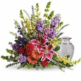 Mixed bouquet with pink lilies, roses, and purple flowers beside a silver urn