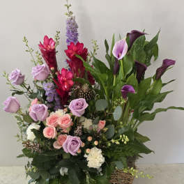 Mixed bouquet with roses, calla lilies, and purple flowers in a woven basket