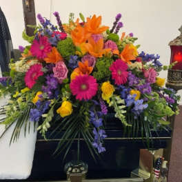 Colorful funeral spray with orange lilies, pink daisies, and purple flowers