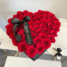 Heart-shaped box filled with red roses and a black ribbon
