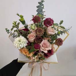 Mixed bouquet of roses and other blooms wrapped in paper with a ribbon