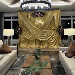 Gold draped event backdrop with floral sprays and a neon Happy Anniversary sign