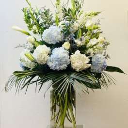Tall white and pale blue floral arrangement in a glass vase