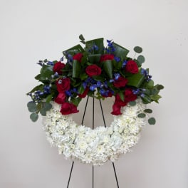 Red roses and blue flowers arranged in a white floral wreath on a stand