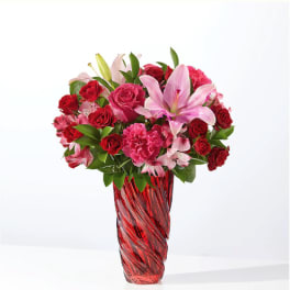 Pink lilies and red roses arranged in a red glass vase