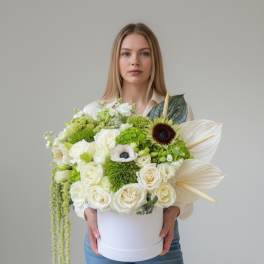 White and green floral arrangement in a round box held by a woman