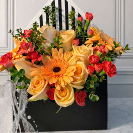 Bouquet of yellow roses, orange gerbera daisies, and red carnations in a black gift box