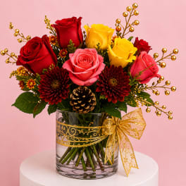 Bouquet of red, pink, and yellow roses in a glass vase with a gold ribbon