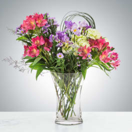 Mixed pink and purple flowers arranged in a clear glass vase