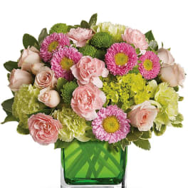 Compact pink and green flower arrangement in a green glass cube vase
