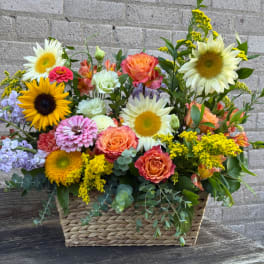 Mixed bouquet in a woven basket with sunflowers, roses, and pastel blooms