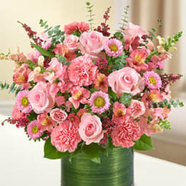 Pink roses, carnations, and mixed flowers in a short green-wrapped glass cylinder vase