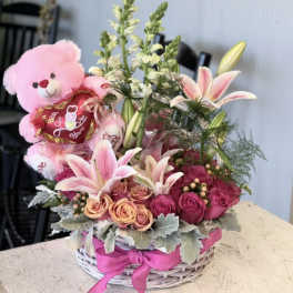 Pink teddy bear in a basket with pink lilies and roses