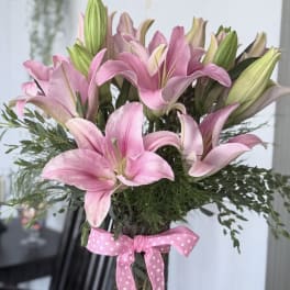 Pink lilies in a clear glass vase tied with a pink polka-dot ribbon.