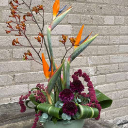 Tall tropical flower arrangement with orange bird-of-paradise blooms in a green container
