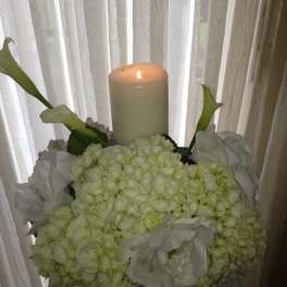 White floral arrangement with a lit pillar candle and calla lilies