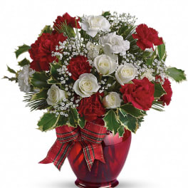 Round arrangement of red carnations and white roses in a red vase with a plaid ribbon bow