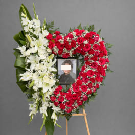 Heart-shaped funeral wreath with red roses and white lilies on an easel