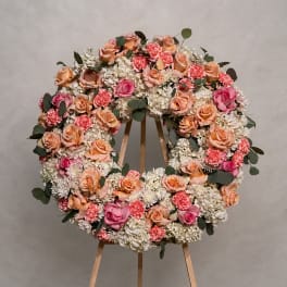 Large circular floral wreath on a wooden stand with pink and peach blooms