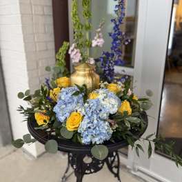 Blue hydrangeas and yellow roses arranged in a gold urn on a black stand