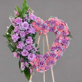 Heart-shaped floral wreath on a wooden stand with pink and purple roses