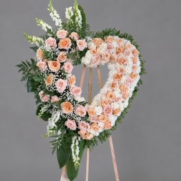 Heart-shaped floral wreath of peach and pink roses on a stand