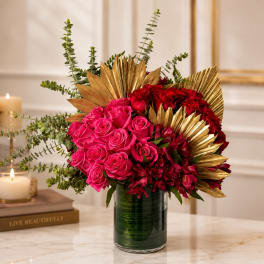 Pink and red roses arranged in a glass vase with gold leaf accents
