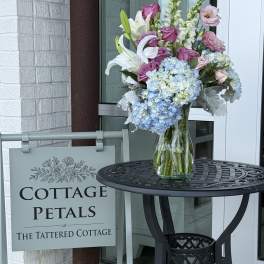 Mixed bouquet in a clear glass vase with lilies, roses, and blue hydrangeas