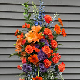 Tall arrangement of orange roses, lilies, and purple flowers