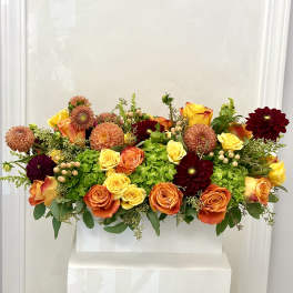 Mixed bouquet of orange, yellow, and burgundy flowers in a white container