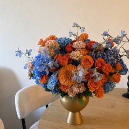 Colorful bouquet of orange, blue, and peach flowers in a gold vase