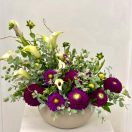 Purple dahlias and pale calla lilies arranged in a white bowl vase
