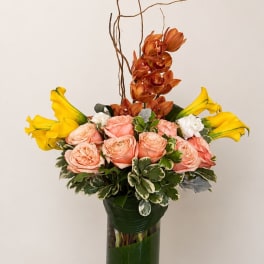 Bouquet of peach roses, yellow calla lilies, and orange orchids in a tall vase