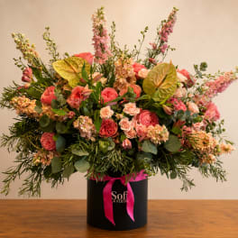 Large pink and peach floral arrangement in a black hatbox with a ribbon