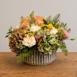 Mixed bouquet of peach roses, hydrangeas, and yellow spray roses in a ceramic vase