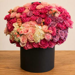 Large round bouquet of pink, peach, and lavender roses in a black box