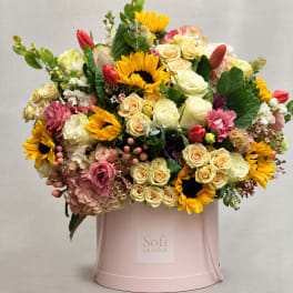 Mixed bouquet of sunflowers, roses, and tulips in a pink hatbox