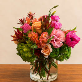 Mixed bouquet of pink, peach, and orange flowers in a clear glass vase