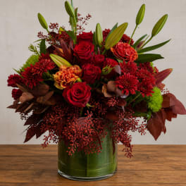 Red roses and lilies in a glass vase with burgundy accents