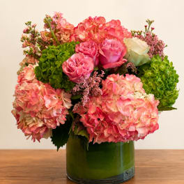 Pink hydrangeas and roses arranged in a green glass vase