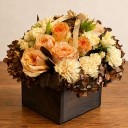 Peach roses and cream carnations in a dark square box with a ribbon