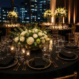 White floral centerpiece on a black-draped banquet table with candles