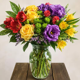 Mixed bouquet of roses, lilies, and purple blooms in a glass vase