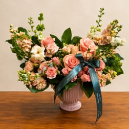 Pink roses and peach flowers arranged in a ribbed vase with a teal ribbon