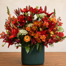 Red and orange mixed flower arrangement in a dark ribbed vase
