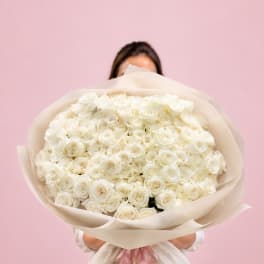 Large bouquet of white roses wrapped in cream paper with a pink ribbon