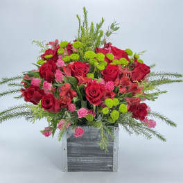 Arrangement of red roses, pink spray roses, and green button mums in a rustic square box.
