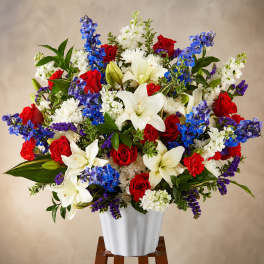 Large bouquet of red roses, white lilies, and blue flowers in a white vase